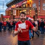 Excited fan holding affordable Liverpool FC tickets in front of the Anfield stadium entrance on matchday.