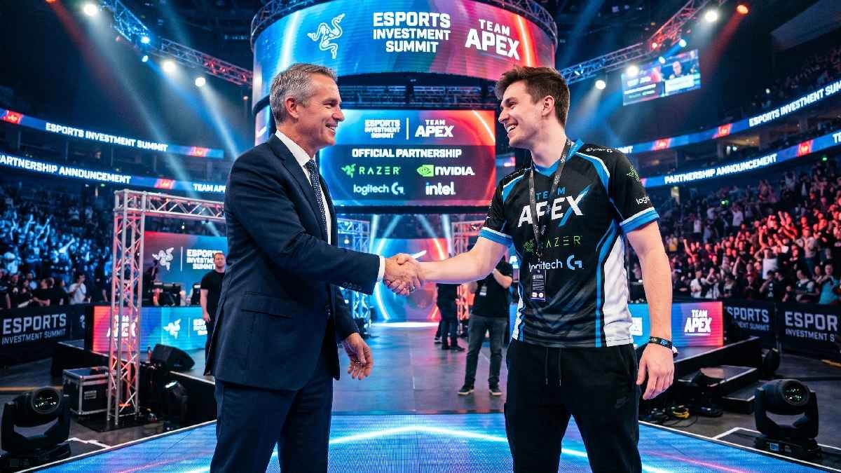 Business executive shaking hands with esports player in arena with large sponsorship banners in background. 