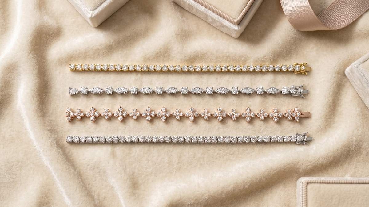 Four diamond bracelets in yellow gold, white gold, rose gold, and platinum displayed on cream velvet surface.