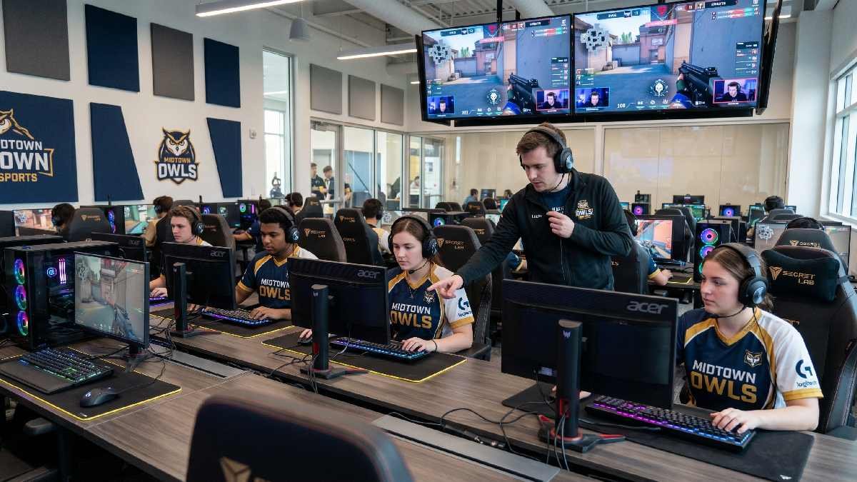 College students in team jerseys practicing esports in a modern university gaming lab with a coach guiding them. 