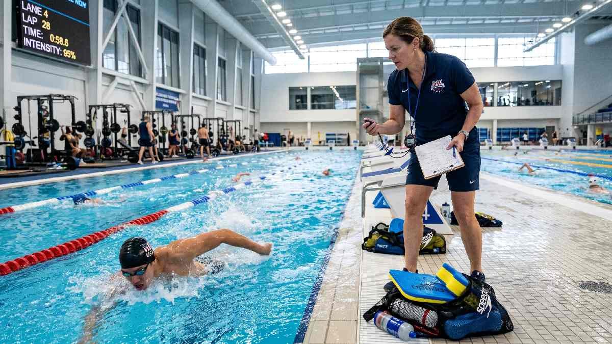 Swim coach timing Olympic swimmer during intense lap training session in a professional aquatic center.