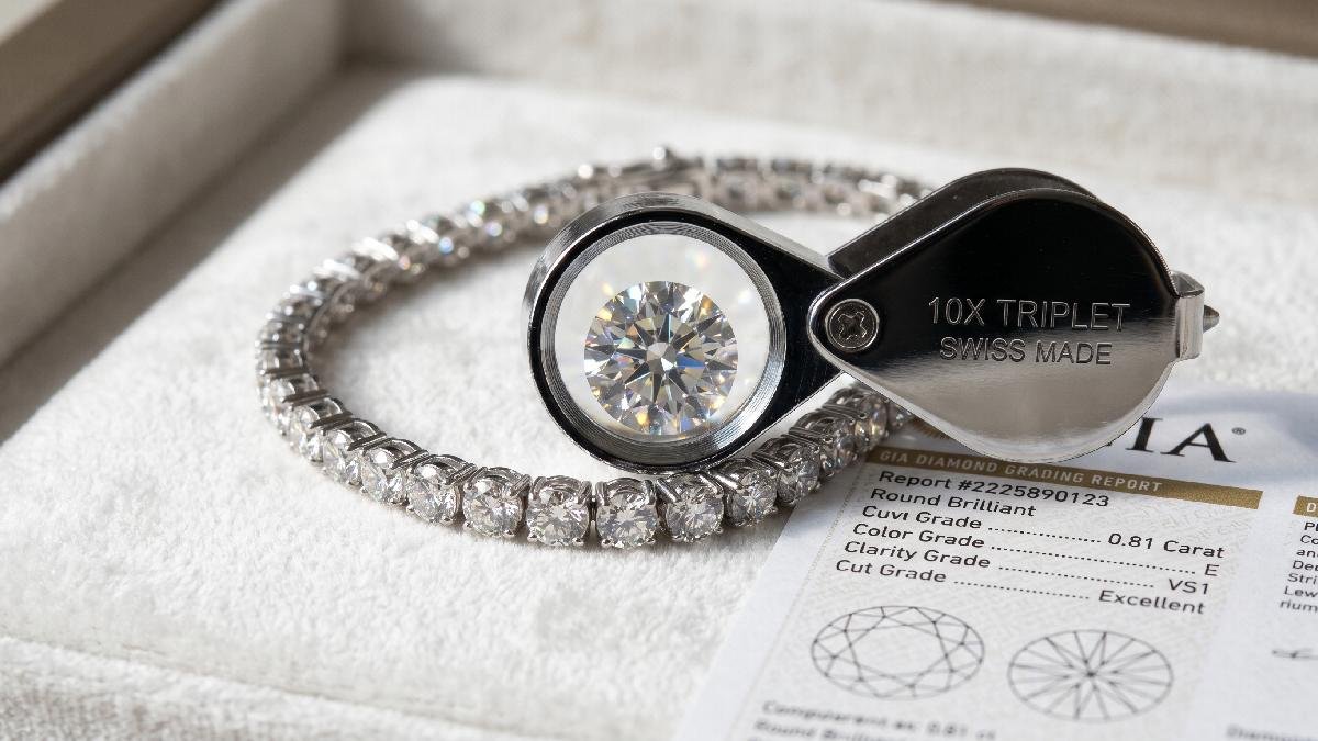 Diamond bracelet on white velvet beside grading certificate and jeweler's loupe showing cut, color, clarity, and carat quality.
