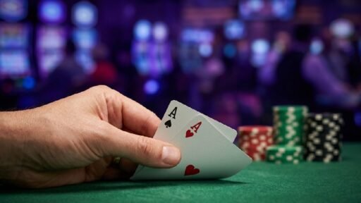 Hand holding two Ace cards over a green felt poker table with colorful chips showing poker in the UK casino style.