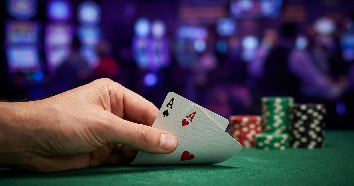 Hand holding two Ace cards over a green felt poker table with colorful chips showing poker in the UK casino style.